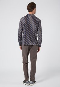 Camisa de manga larga de estampado en azul marino, con un diseño geométrico en azul, rojo y beige; combinada con pantalones tailored color marrón claro y zapatillas casuales.