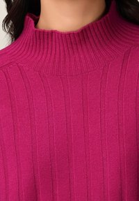 Pull côtelé fuchsia avec un col montant. La texture est douce et tricotée, avec des lignes verticales pour une apparence structurée.