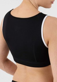 Bra sportivo nero con bordature bianche, dotato di scollatura arrotondata e cuciture sagomate per un design aderente. Texture liscia, senza hardware visibile.
