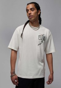 Weißes oversized T-Shirt aus Baumwolle, mit einem schwarzen Grafikdruck eines Basketballkorbs auf der linken Brustseite. Kurze Ärmel, lockere Passform.