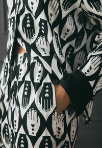 Set de loungewear alb-negru cu un design modelat manual. Material moale, croi lejer și talie elastică cu detalii de buzunar.