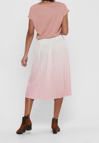 Falda midi plisada rosa con un degradado blanco, combinada con una blusa corta de mangas, brillante y rosa, y botas marrones hasta el tobillo con tacón cuadrado.