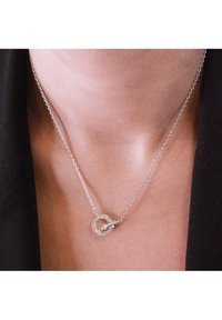 Collana d'argento con un pendente circolare, caratterizzato da un design a torsione e incastonato con piccole pietre trasparenti, sospeso su una catena sottile.