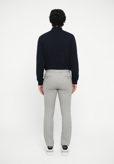 Top de manga larga azul marino y pantalones ajustados gris claro, con detalles en la parte de atrás. El modelo lleva zapatillas blancas con acentos negros.