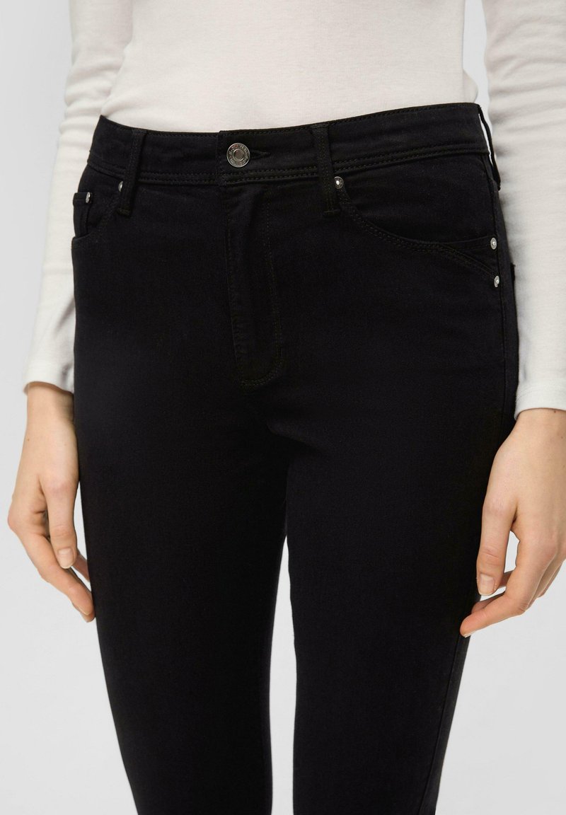 Schwarze Denim-Jeans mit schmaler Passform, Fünf-Taschen-Design und silbernen Beschlägen an der Vorderseite. Der Stoff hat eine glatte Textur und minimale Nähte.