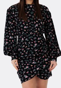 Svart blommig klänning med rosa och gröna blommor, långa puffärm, rund halsringning och en omlott-längd. Mjuk textur.