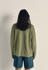 Langærmet skjorte i olivengrøn i en afslappet pasform, parret med blå denimshorts, der fremhæver stofstruktur og afslappet stil.