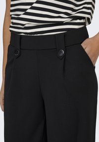 Sorte skræddersyede bukser med en glat tekstur, med en tilpasset talje, dobbelte knapdetaljer og sidelommer, kombineret med en stribet top.