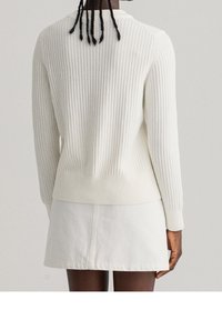 Svetle béžový žebrovaný svetr s dlouhými rukávy, kulatým výstřihem a texturovaným povrchem. V kombinaci s bílou džínsovou sukní.