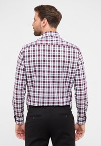 Camicia button-up con motivo a quadri bordeaux, bianco e blu navy. Maniche lunghe, colletto classico e silhouette aderente. Pantaloni neri visibili.