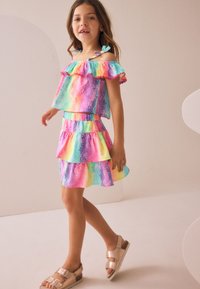 Flerfärgad klänning i lager med axelbandslös volangtopp i rosa, blått och gult. Kombinerad med ljusa sandaler.