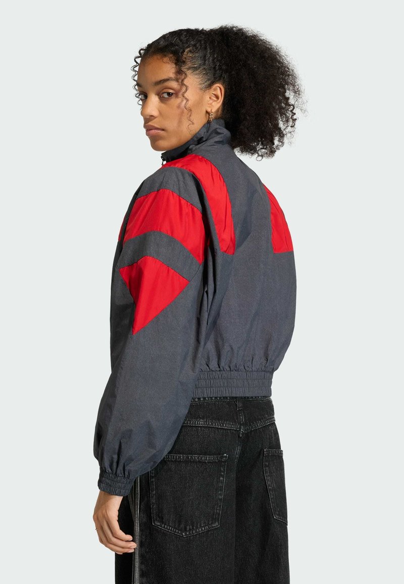 Grau Windbreaker-Jacke mit roten Akzenten. Sie verfügt über einen hohen Kragen, einen elastischen Bund und gepuffte Ärmel mit Zickzackmustern.