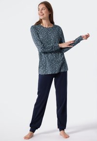 Long-sleeve top in teal with black speckles, paired with navy trousers. Soft fabric, relaxed fit, and ribbed cuffs on sleeves.