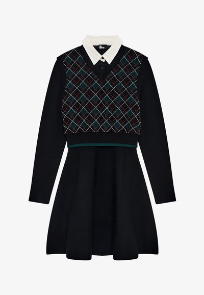 Vestido preto de manga longa com colarinho branco pontudo e colete sem mangas de padrão argyle em verde escuro, vermelho e branco.