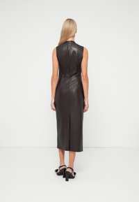Zwart leren mouwloos jurkje met een hoge halslijn, aansluitende silhouet, ritssluiting aan de achterkant en een split aan de zoom. Glad textuur.