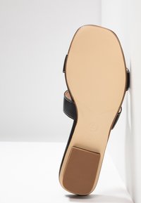 Black leather sandal sole with a smooth texture, flat design, and contrasting stitching. Features a rounded toe and a logo imprint.