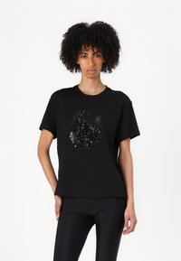 T-shirt nera in cotone a maniche corte con un design testurizzato di foglie in sequins disposte in un motivo circolare nella parte anteriore.