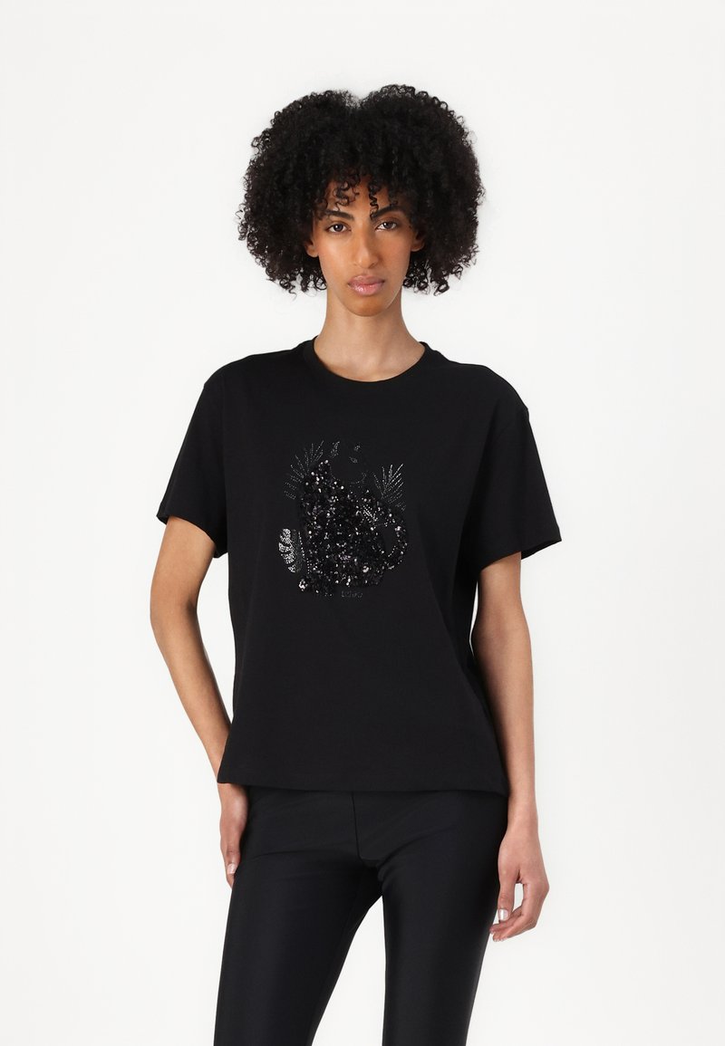 T-shirt nera in cotone a maniche corte con un design testurizzato di foglie in sequins disposte in un motivo circolare nella parte anteriore.