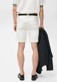 Pantaloni in denim bianco con risvolti, tasche posteriori e una cintura in pelle nera. Il modello tiene in mano una giacca nera, mostrando un look casual.