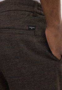Bruine geweven broek met een textuurpatroon en een zwart merklabel op de achterzak. Heeft een klassieke snit en een op maat gemaakte uitstraling.