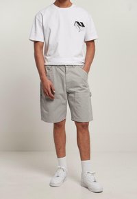 T-shirt bianca in cotone con grafica della tasca nera, abbinata a pantaloni cargo grigi chiari con tasche laterali e vita elastica. Sneakers bianche.