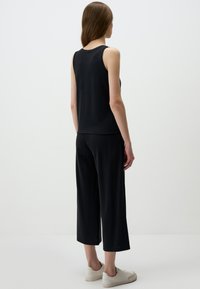 Top nero senza maniche abbinato a culotte nere ampie, con una texture liscia e una vestibilità rilassata. Indossato con sneaker bianche.