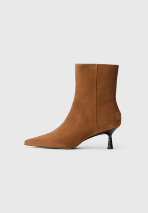 Brown suede ankle boot with a pointed toe and a conical black heel. Smooth texture with minimal detailing and a clean silhouette.