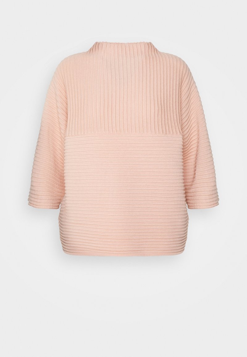 Pull côtelé rose clair avec un col montant, des manches trois-quarts et une coupe décontractée et carrée. La texture est douce et texturée.
