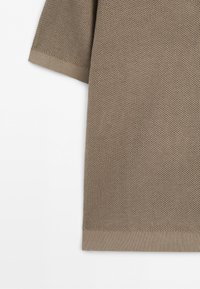 Gros plan d’un tissu tricoté beige avec manches courtes et ourlet côtelé sur fond blanc uni.