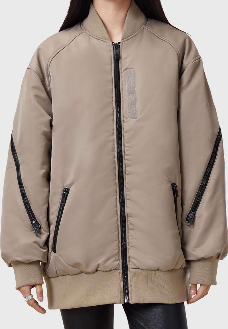 Khaki Bomberjacke mit glatter Textur, Reißverschlusstaschen und elastischen Bündchen. Verfügt über einen gerippten Kragen und ein dezentes Stoffpatch-Detail.