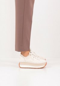 Λευκά αθλητικά παπούτσια με δαντελωτό σχέδιο, χοντρή λευκή πλατφόρμα και τραχιά λαστιχένια σόλα. Συνδυασμένα με καφέ ραμμένα παντελόνια.