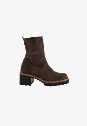 Stivale alla caviglia in suede marrone con suola nera spessa, punta tonda e bordo decorativo cucito. Presenta un linguetta sul retro per una facile calzata.