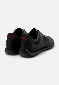Scarpe da ginnastica nere con una parte superiore testurizzata, caratterizzate da pannelli in mesh. Il tallone presenta un logo "Camper" rosso in rilievo. Design della suola leggero e flessibile.