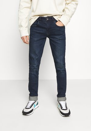 Donkerblauwe denim jeans met een slim fit, voorzien van een knoopsluiting, zijzakken en opgerolde boorden. Draagt bij multicolore sportschoenen.