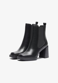 Bottines en cuir noir avec des panneaux élastiques sur les côtés, un talon bloc, et une finition lisse avec un minimum de détails et un bout arrondi.