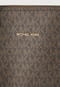 Portefeuille Michael Kors en matériau brun texturé avec un motif géométrique. Logo doré affiché en évidence sur la surface.
