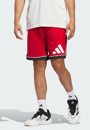 Red athletic shorts with black trim, featuring a white diagonal logo on the left leg. Paired with black and white sneakers and white socks.