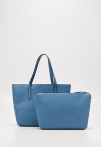 Sininen olkalaukku kahdella kahvalla, tasainen nahkamainen materiaali. Mukana on yhteensopiva vetoketjullinen pussukka, molemmat yhtenäisessä sinisessä sävyssä.