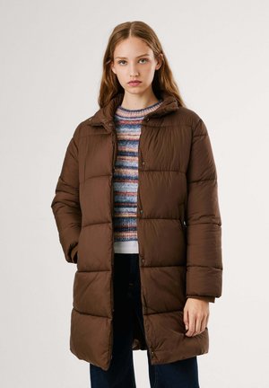 Manteau rembourré marron avec un col haut, des boutons-pression et une texture de carrés matelassés. Porté sur un pull à rayures multicolores.