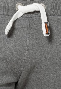 Pantalones de chándal de algodón gris con cordón blanco, ojales de metal y una etiqueta negra y naranja cosida en la cintura.