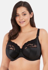 Reggiseno nero con ferretto, caratterizzato da un sovrapposto in pizzo sulle coppe, lati in satin lisci, spalline regolabili e un fiocco al centro.