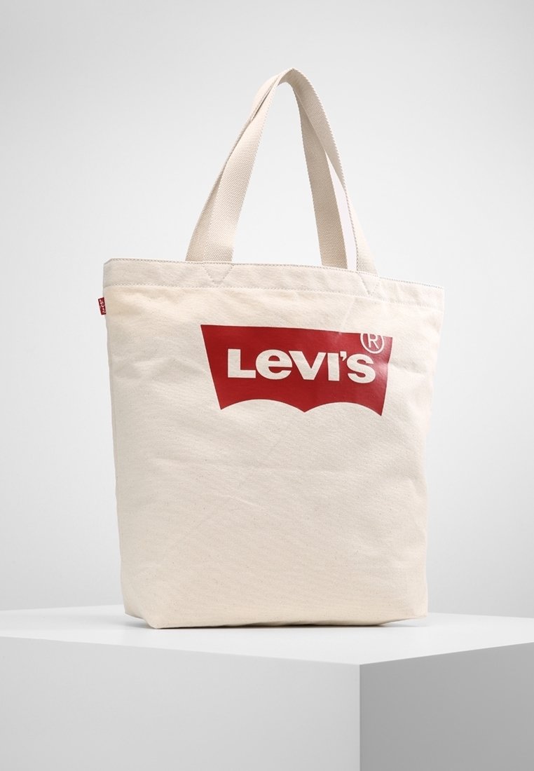 Beige canvas axelväska med röd Levi's-logotyp, två handtag upptill, fyrkantig form och slät yta. Inga ytterligare dekorationer eller mönster.