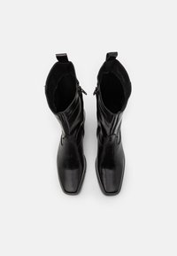 Botas negras de cuero hasta el tobillo con punta cuadrada, textura suave, cremalleras laterales y tiradores en el cuello para ponerse y quitarse fácilmente.