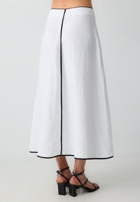 Jupe maxi en lin blanc avec des bordures noires le long de l'ourlet et de la couture arrière. Elle présente une taille ajustée et une silhouette fluide.