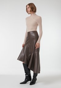 Haut à manches longues beige en tissu doux, associé à une jupe en cuir marron foncé avec un ourlet évasé et des bottes noires jusqu'aux genoux.