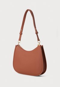 Saco de ombro em couro castanho com fundo curvado, hardware dourado e alça ajustável, colocado sobre um fundo neutro.