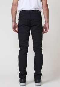 Črne jeans hlače s ožjim krojem, dizajnom s petimi žepi in kontrastnimi šivi. Imajo gladko teksturo in diskretne strojne dodatke.