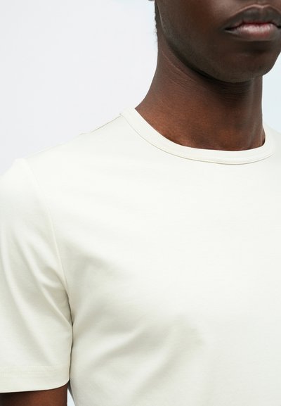 Hele beež värviga lühikeste varrukatega särk, mis on valmistatud pehmest puuvillast. Särgil on ümmargune kaelus ja sile tekstuur, millel on minimaalsed õmbluse detailid.