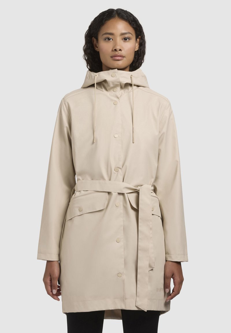 Cappotto impermeabile color sabbia con cappuccio, bottoni a pressione, cordoncino regolabile, vita con cintura e tasche frontali. Tessuto liscio e design fino al ginocchio.