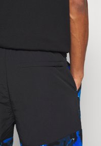 Pantalones cortos negros, ligeros y con un acabado texturizado. Con un bolsillo lateral con cremallera y una cinturilla negra, combinados con una camiseta negra lisa.